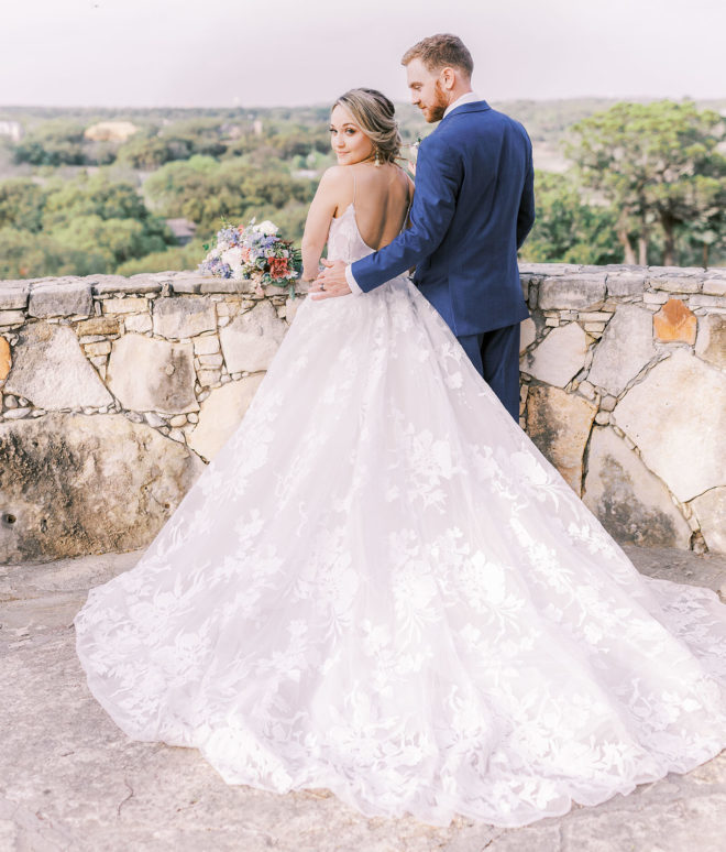 Al fresco scene of Bride and groom looking at Texas Hill Country views with bride looking directly at camera while groom looks at her