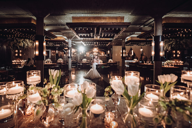 Bride and groom slow dancing in the distance of an empty industrial chic hall of the Astorian