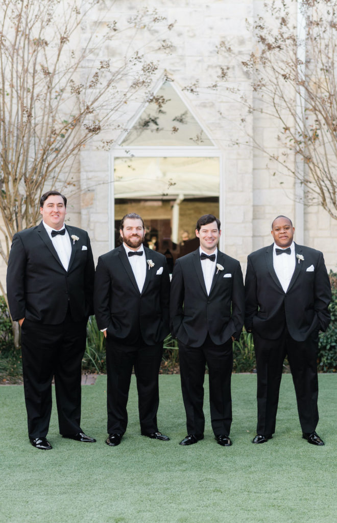 Groomsmen in black tuxes with blush and wine florals. 