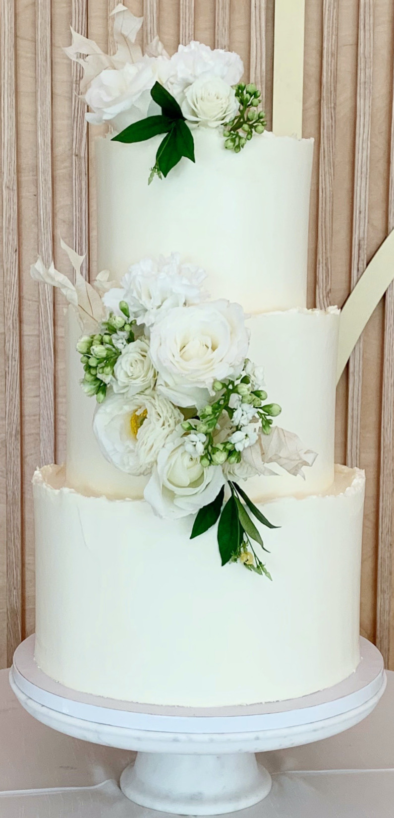 Three tiered ivory cake with rough edge and white floral decor