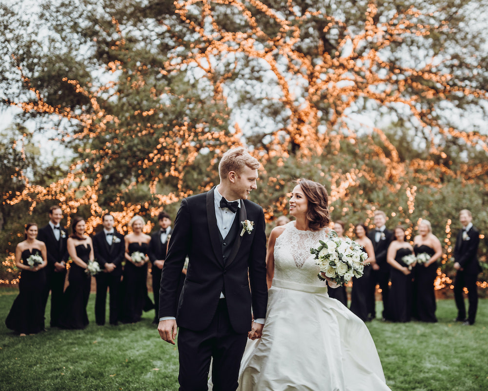 Bride and groom holding hands and smiling, with wedding party in the background at The Houstonian Hotel, Club & Spa.