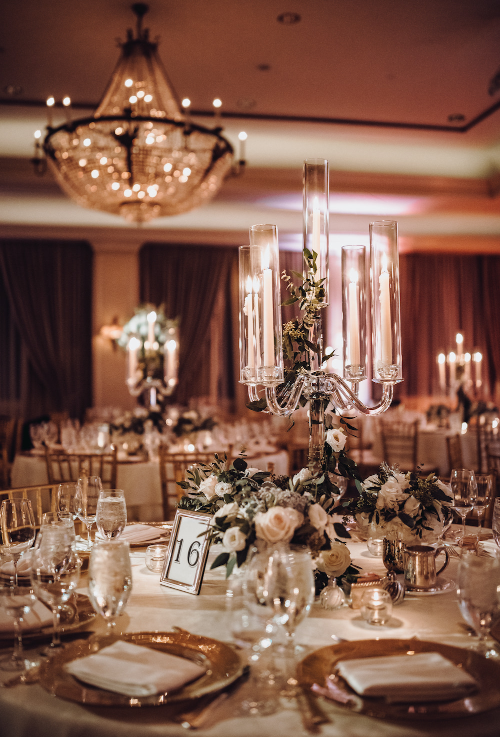 Table setting with small blush rose floral centerpiece, tall glass candelabras and gold chargers in the ballroom of the Houstonian Hotel Club & Spa. 