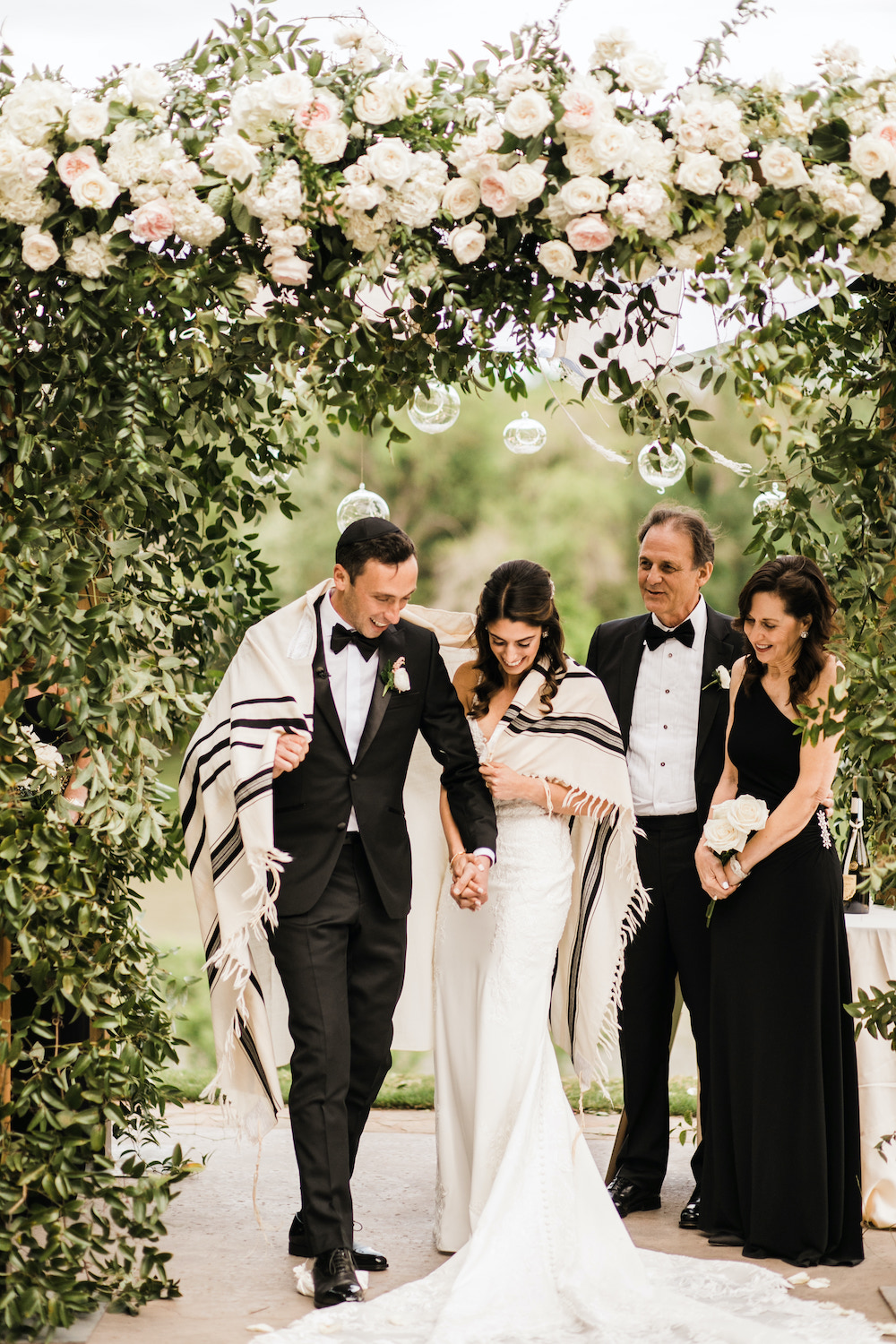 Bride and groom holding hands making their way down the aisle after the ceremony with their family pictured behind them. 