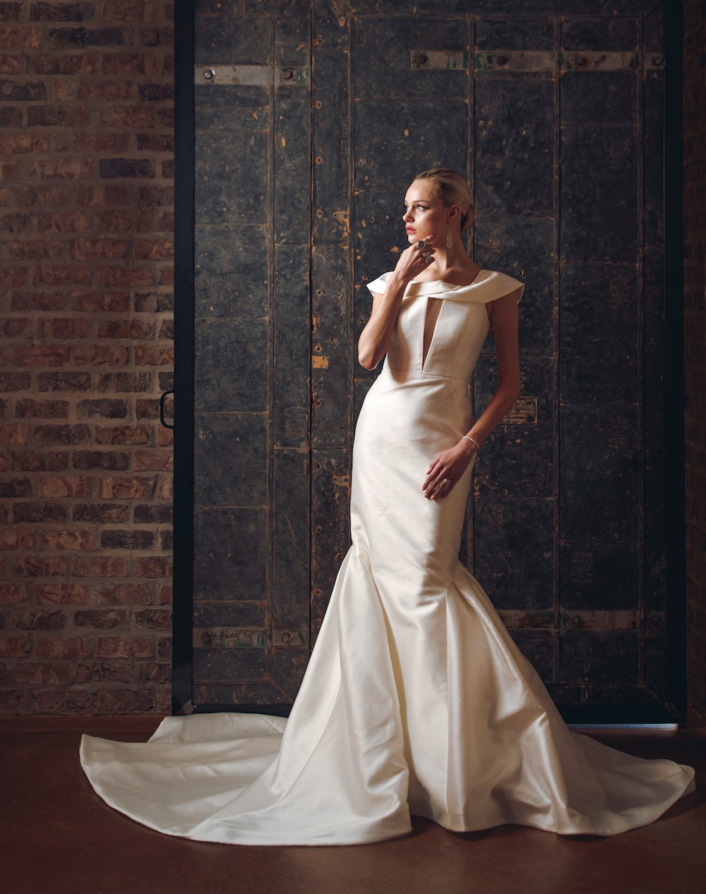 Model is wearing a cream satin wedding gown that drapes to the floor in the wedding venue, Iron Manor in Conroe, Texas.