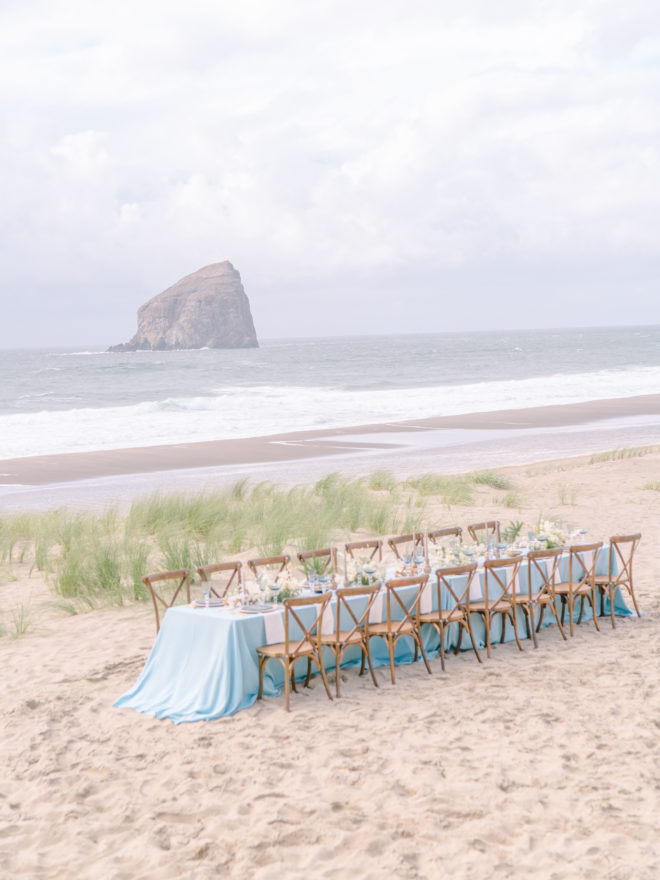 A lone, long wedding reception table with a flowy blue tablecloth sits on Cannon Beach.