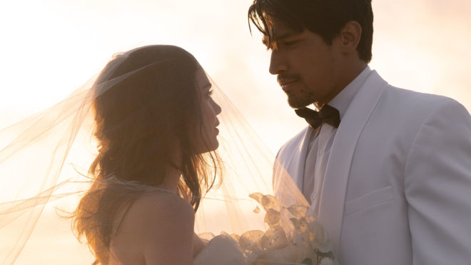 The model newlyweds gaze into each others eyes after the beach wedding as the sun sets behind them.