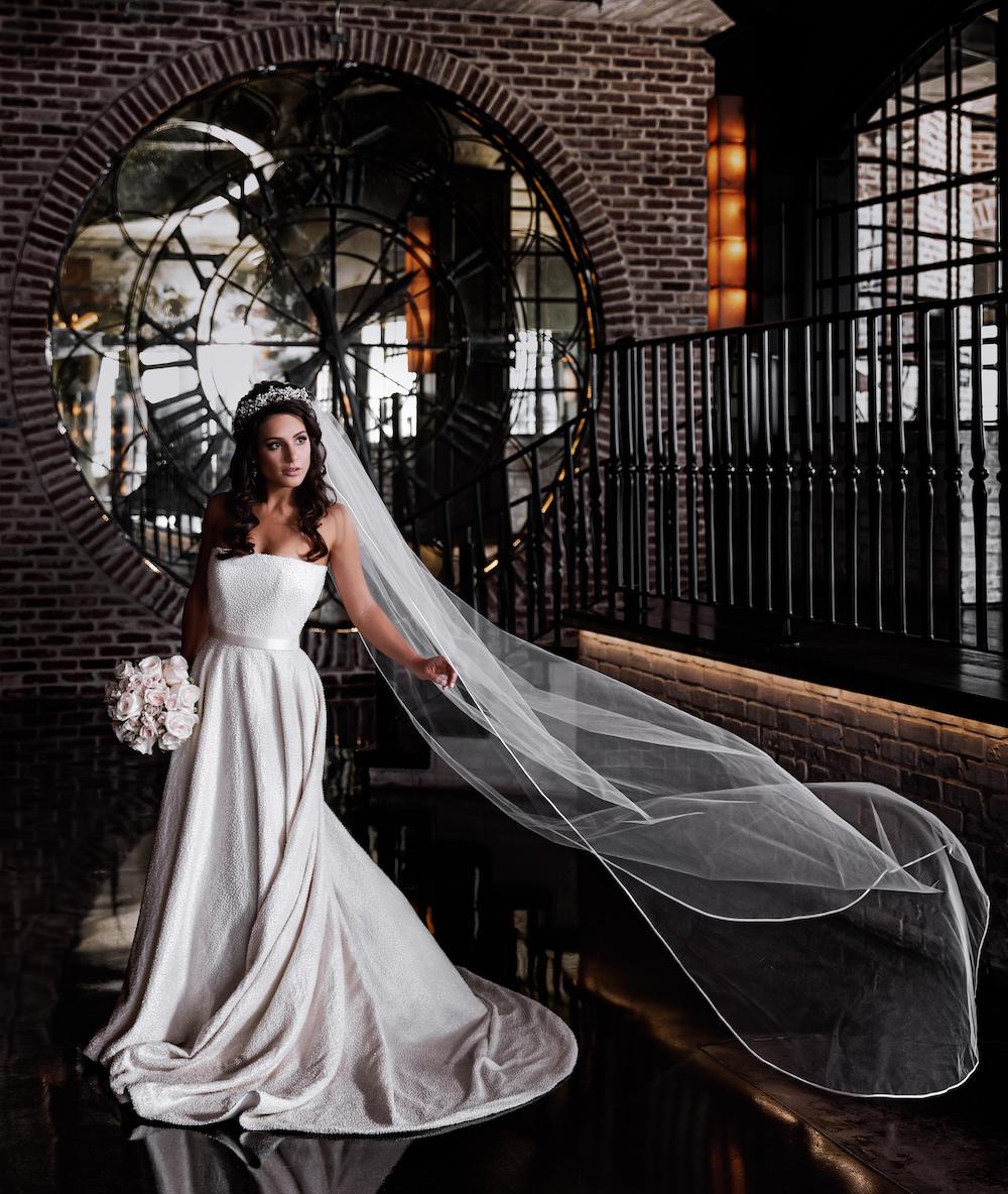 The bride's veil flows elegantly as she poses holding her wedding bouquet at The Astorian.