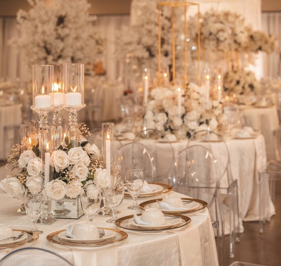 White wedding reception dinner with glass candle holders and pillar candles.