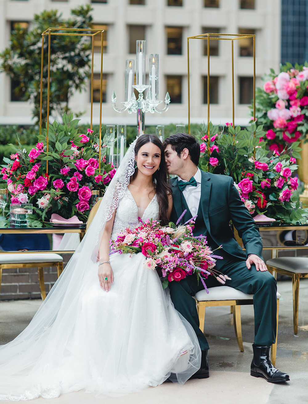 The groom in an emerald suit whispers sweet nothings to his bride while she holds her vibrant bridal bouquet.