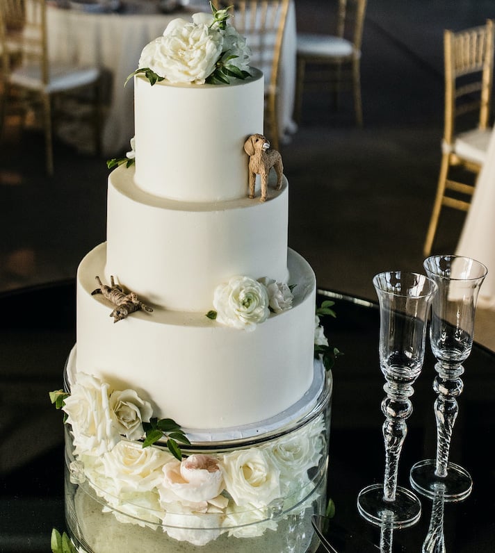 Elegant three-tier cake with pearlized icing and florals designed by Sweet Treats Baker, including adorable replicas of the bride and groom's pet cat and dog.