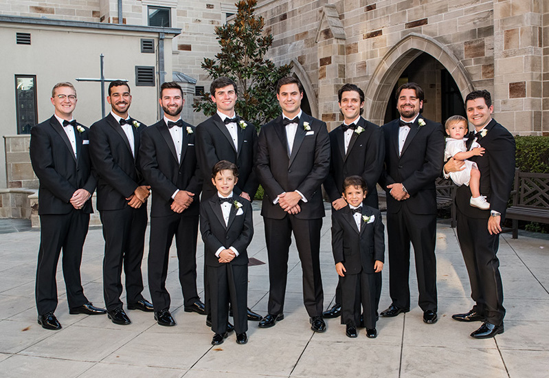 Groomsmen and groom outside of chapel wearing classic tuxedoes and black bow ties. 