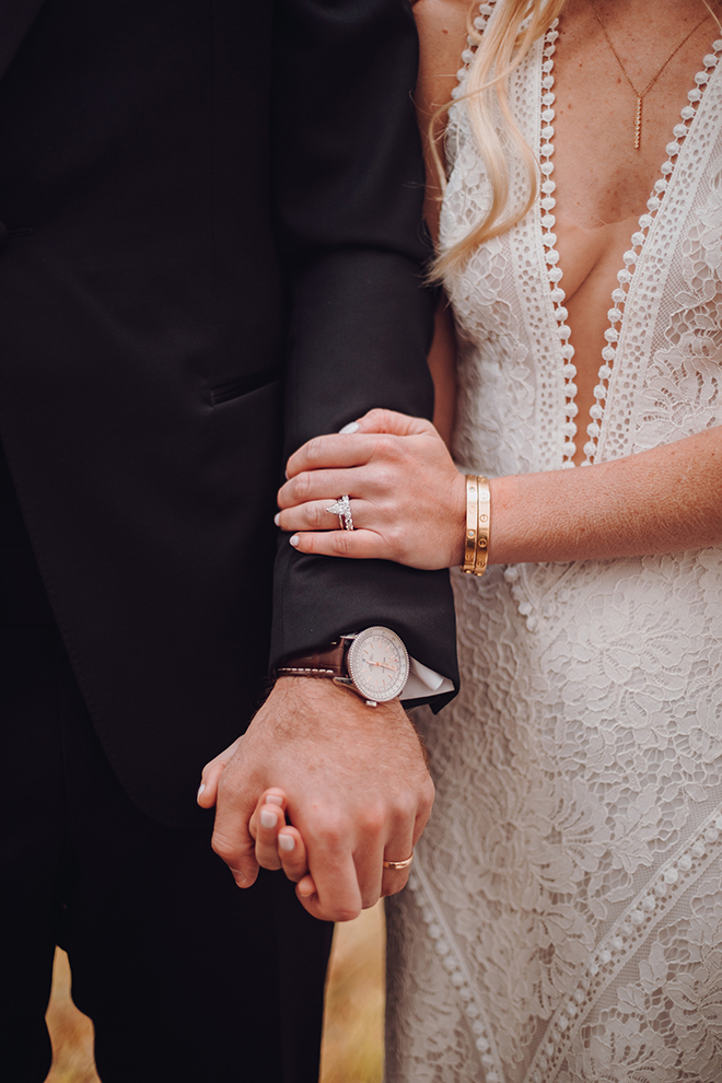 A bride in a plunging neckline wedding dress holds hands with her groom, showing their wedding bands after saying "I do."