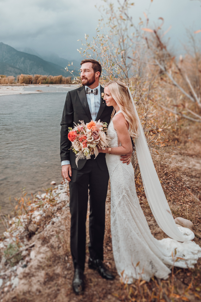 The bride and groom embrace overlooking the Snake River in Jackson, Wyoming while the bride holds her fall wedding bouquet.