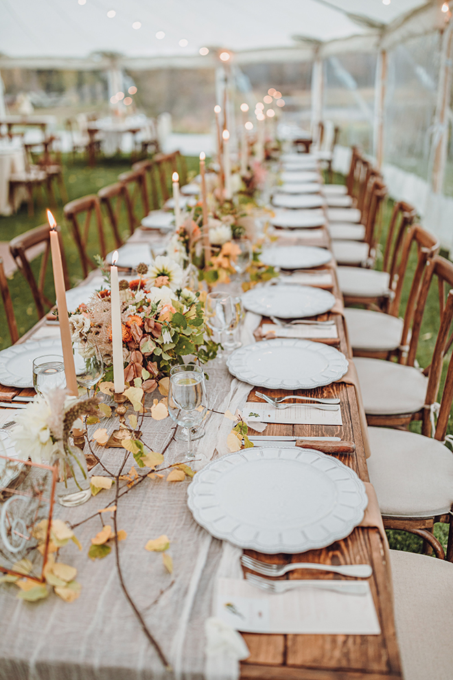 A long table is decorated with bud vases, aspen sprigs, and tall candlesticks during a tented reception.