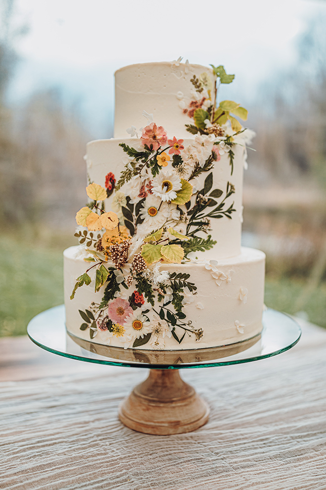 A beautiful rustic-inspired ivory three-tiered wedding cake features wildflowers cascading down its front.