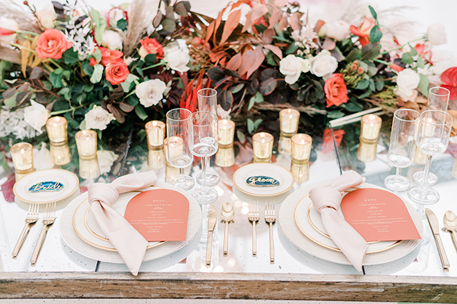 A closeup of the brides and grooms reception table with vibrant florals, coral-colored menus, and teal agate slices that say bride and groom.