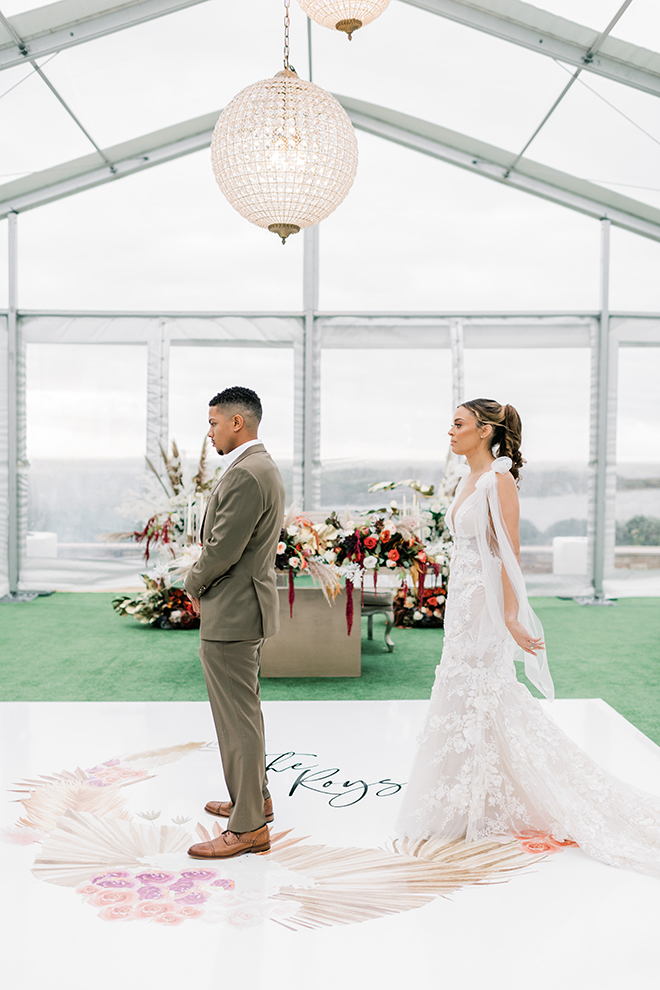 The bride stands behind her groom before the first look inside a decorated tent.