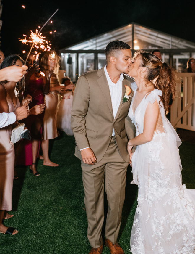 Bride and groom kissing during a night time sparkler send-off outside the tented wedding reception on a private property next to Galveston Bay in Texas.