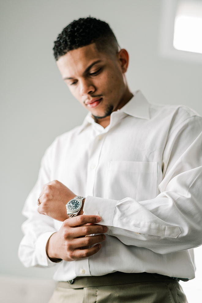 The groom gets ready for his wedding, buttoning his shirt cuff.