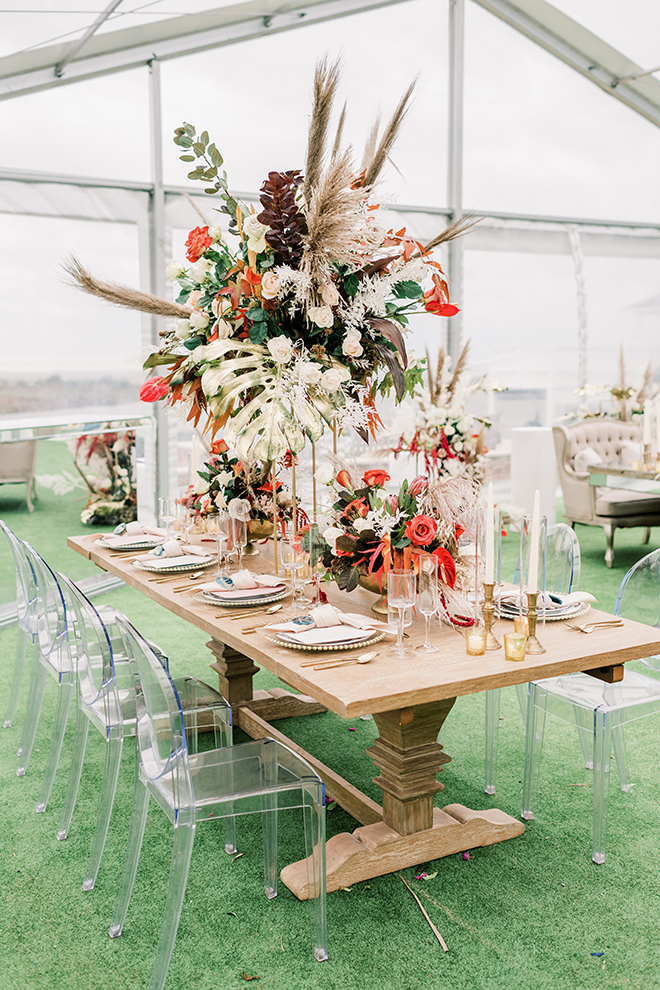 A beautiful tablescape at this sunset colored wedding is bursting with vibrant, cascading floral arrangements boasting orange, red, and blush blooms.