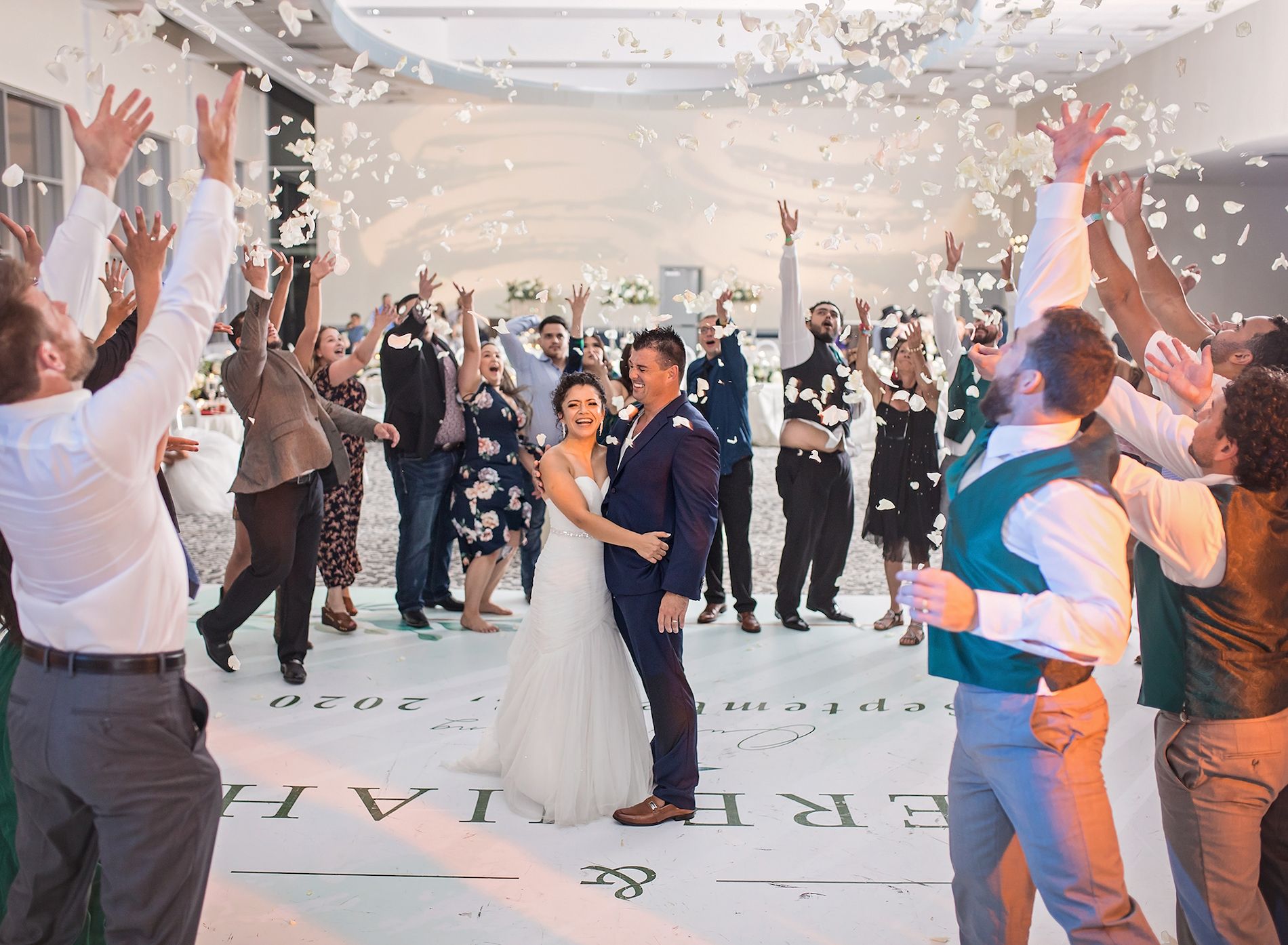 Friends and family circle around the bride and groom on the dance floor and throw white rose petals up in the air towards them to celebrate.