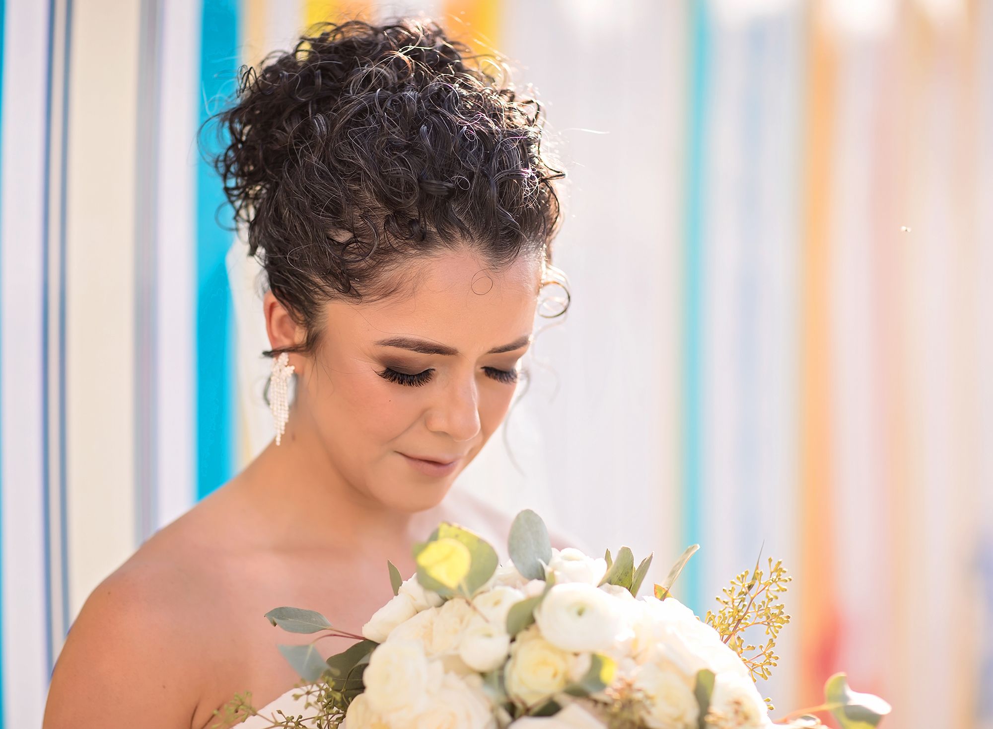 A bride tilts her head down looking at a bridal bouquet in front of a colorful array of classic surfboards at her lakeside wedding at Margaritaville Resort, Lake Conroe.