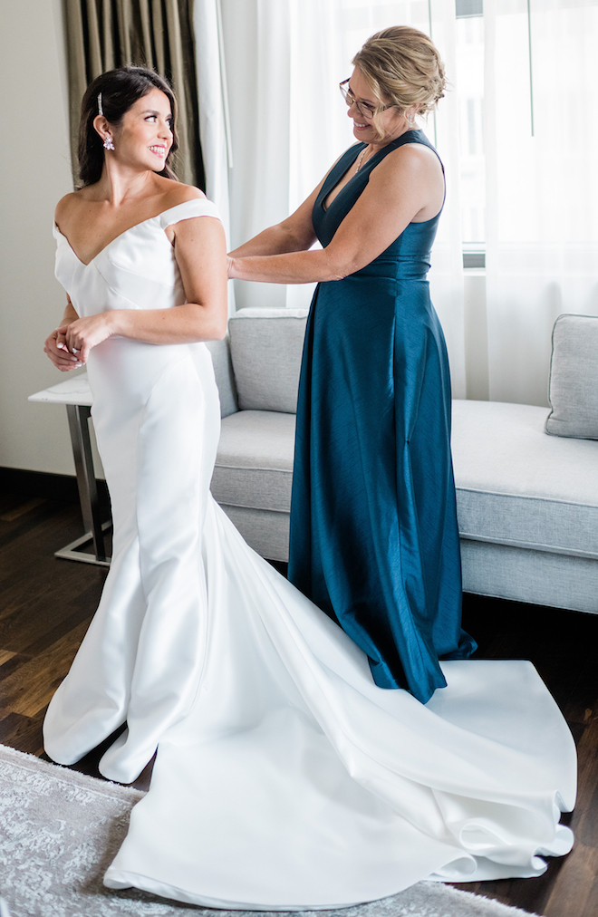 The bride smiles at her mom as she is putting on her wedding dress.