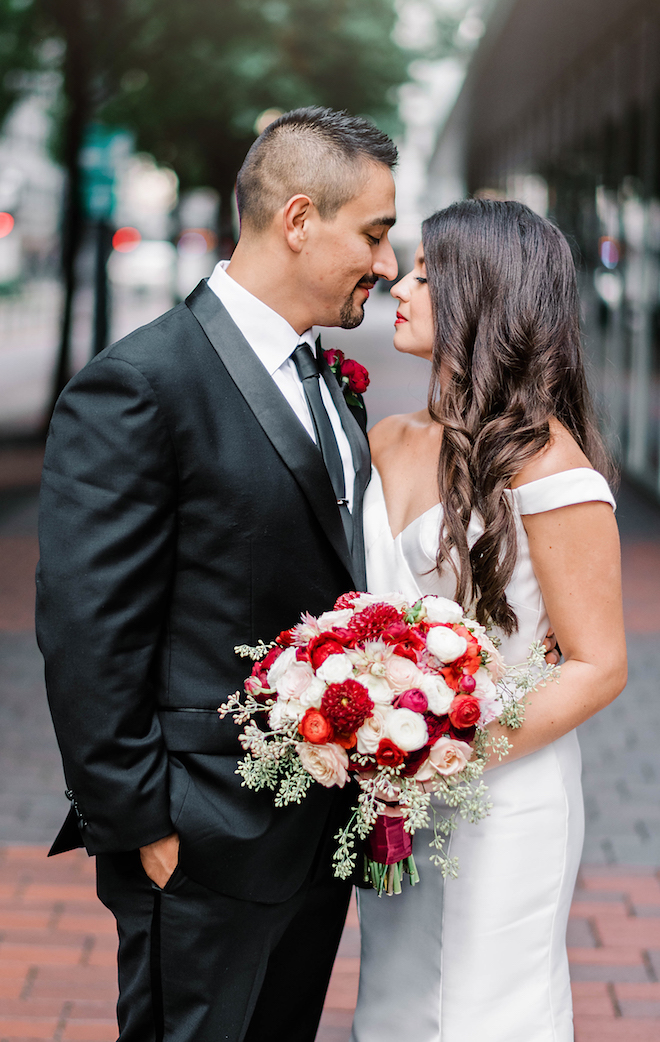 Bride is holding her ruby red bridal bouquet with her husband by her side.