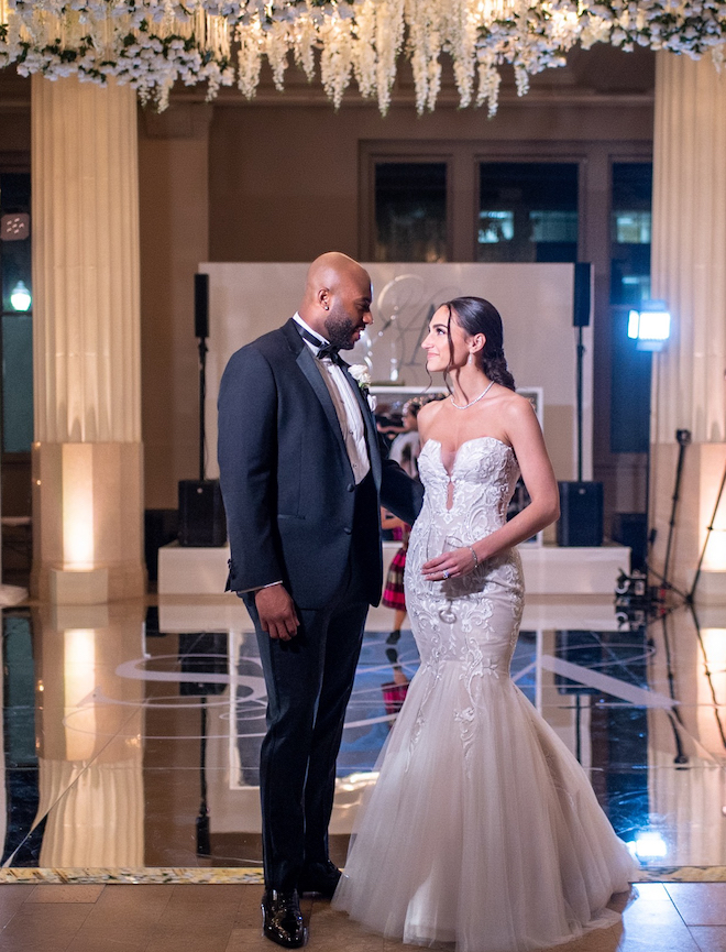 Groom looks at bride while holding her, and she looks back up at him with a smile. 