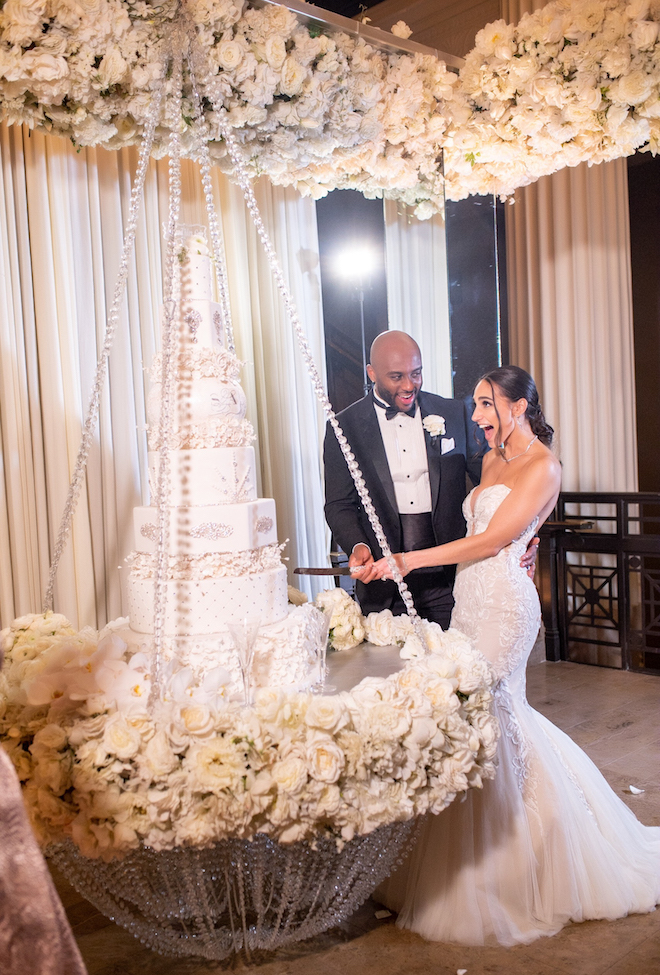 Bride and groom cut their six tiered cake, while the bride drops her jaw in excitement. 