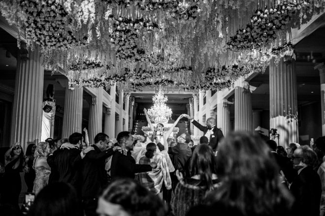 Bride and groom throw up their hands with excitement as they dance the night away in a room full of family and friends.