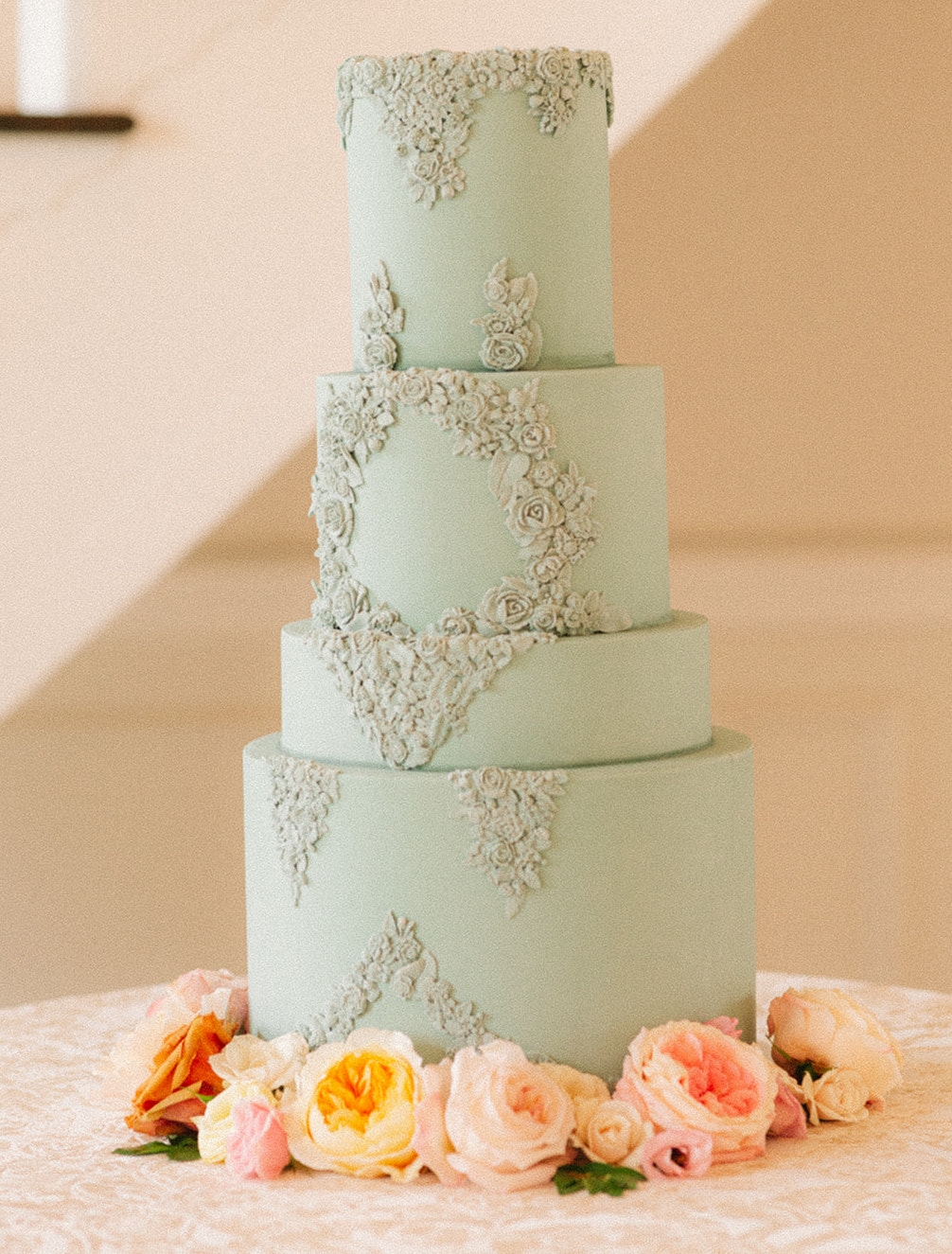 4-tiered wedding cake with sage green frosting with artfully curated flowers at the base.