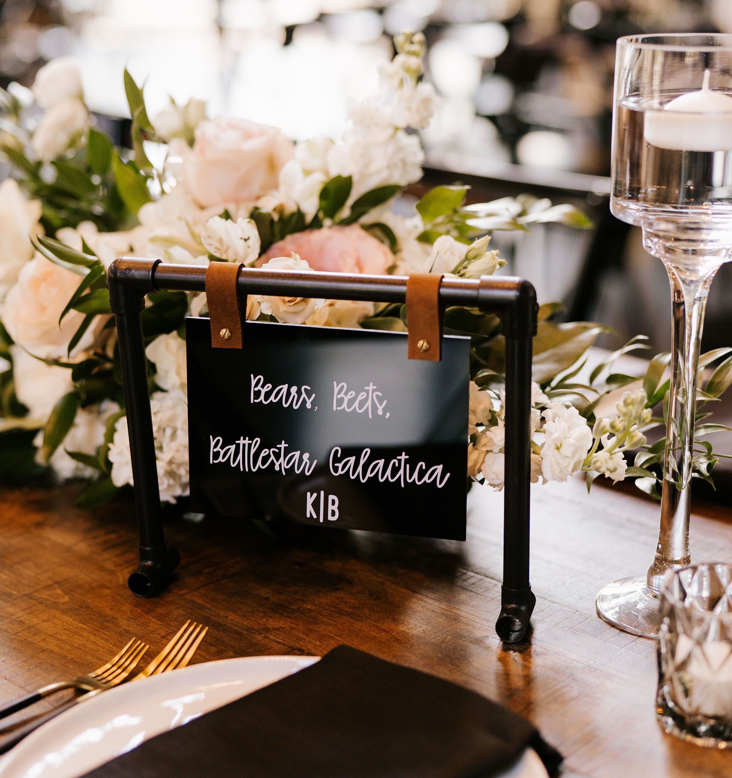 Custom industrial chic wedding table cards made of faux-iron pipe, acrylic, and leather straps display the couple's creative table names.