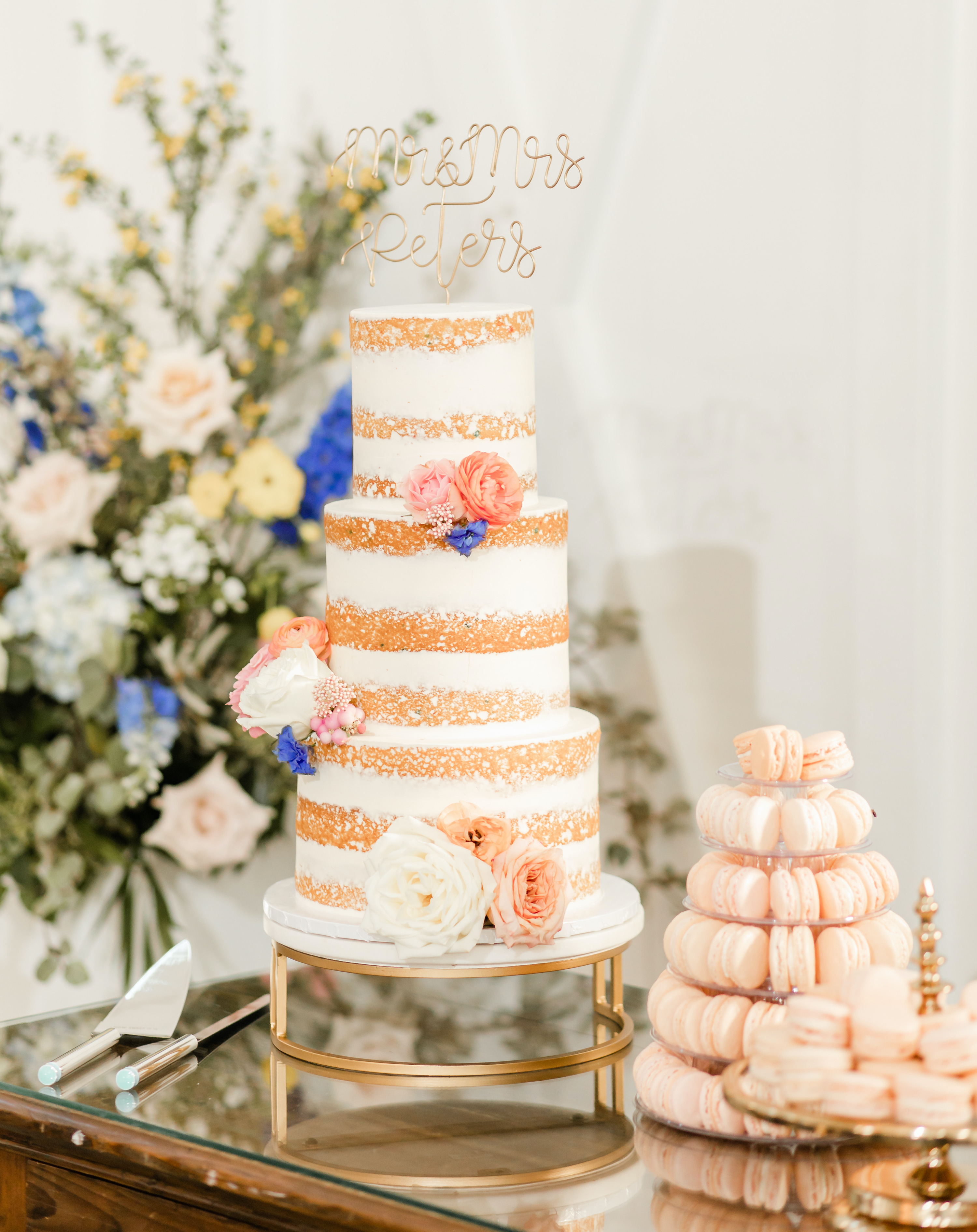 A beautiful cake with white frosting and peach macarons next to it.