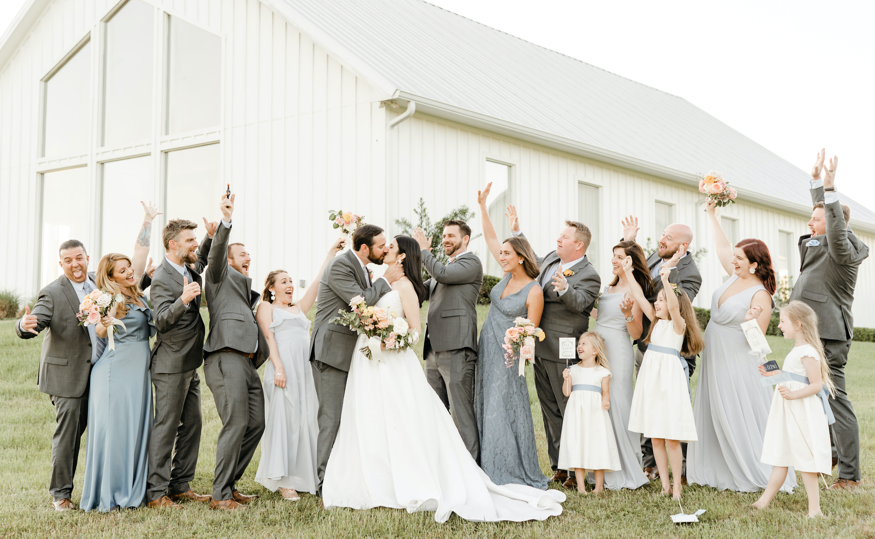 The bride and groom kiss with their friends surrounding them.