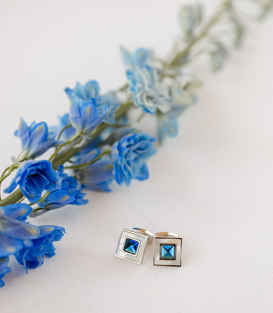 The groom's cuff links have a vibrant blue gem and sit next to a piece of Delphinium.