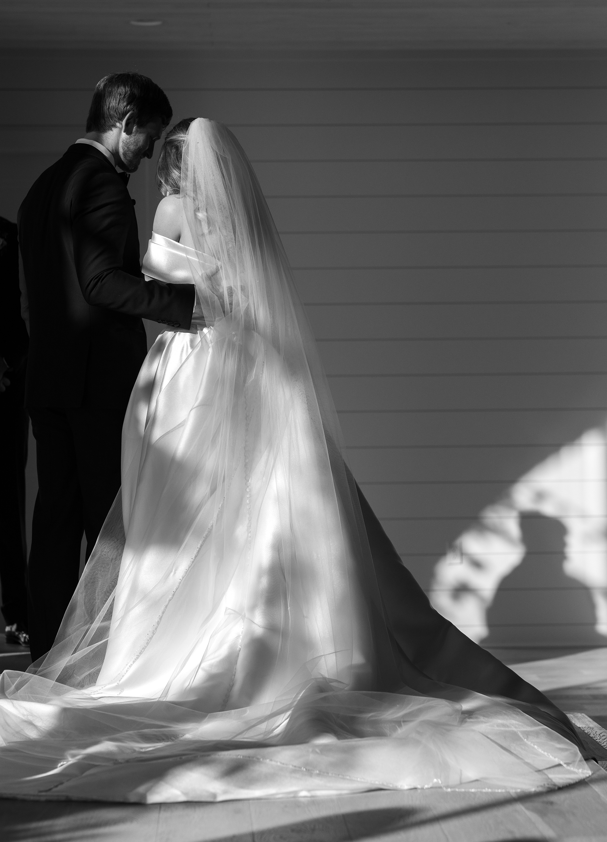 A black and white photo of the bride and groom's back with the sunlight shining onto them.