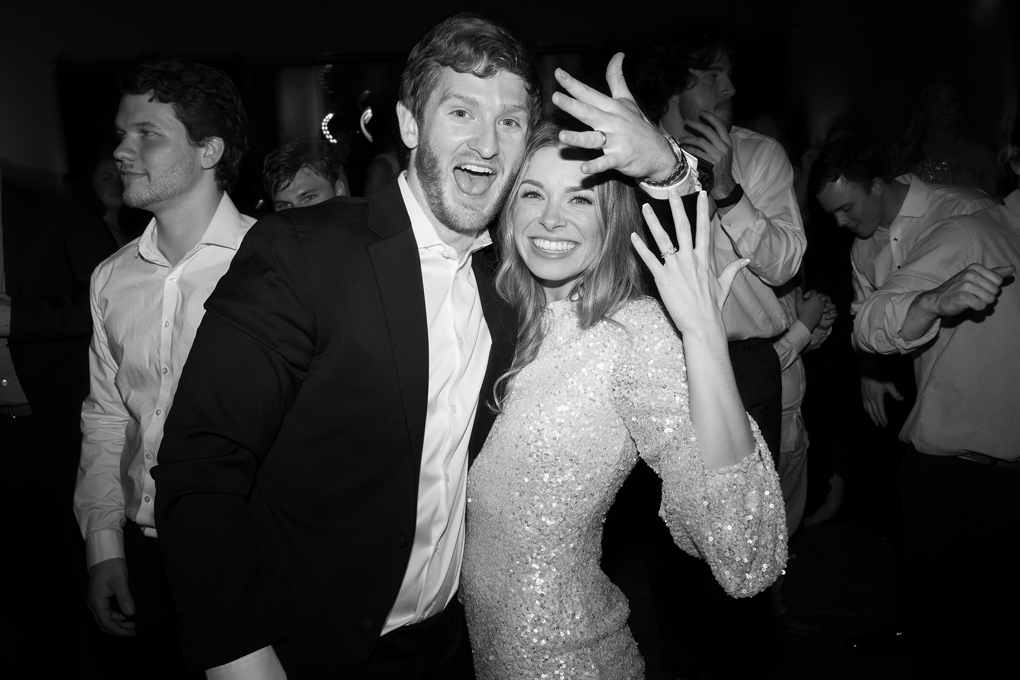 The bride and groom hold up their hands to show their wedding rings at the reception.