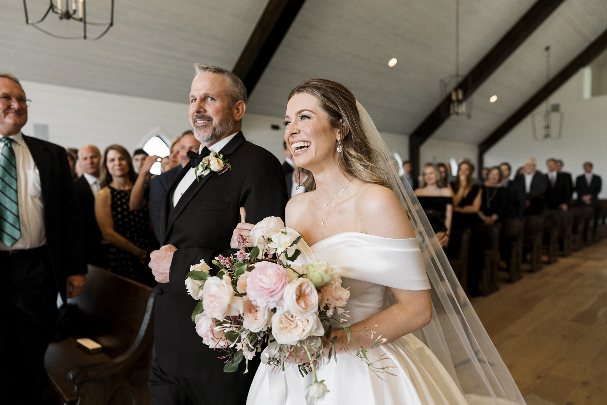 The bride is smiling while her dad walks her down the aisle at her wedding.