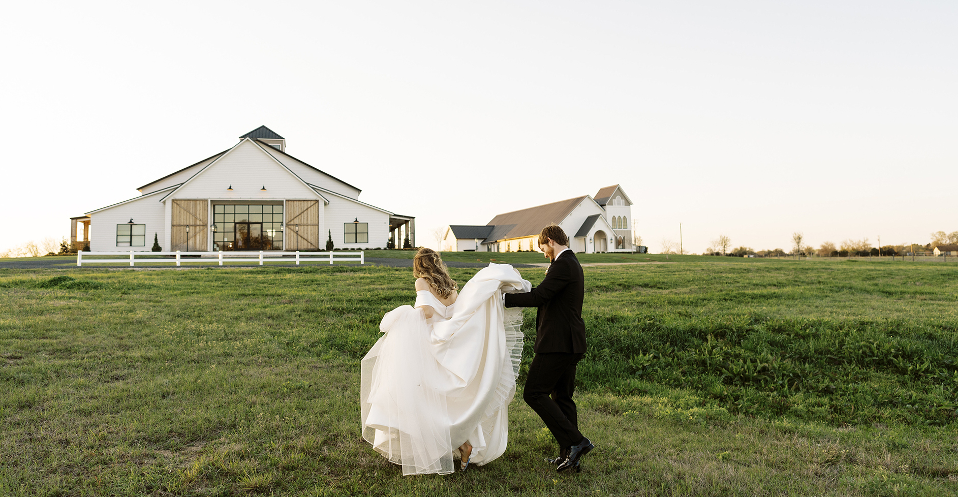 The groom holds the brides dress as they walk towards the wedding venue.