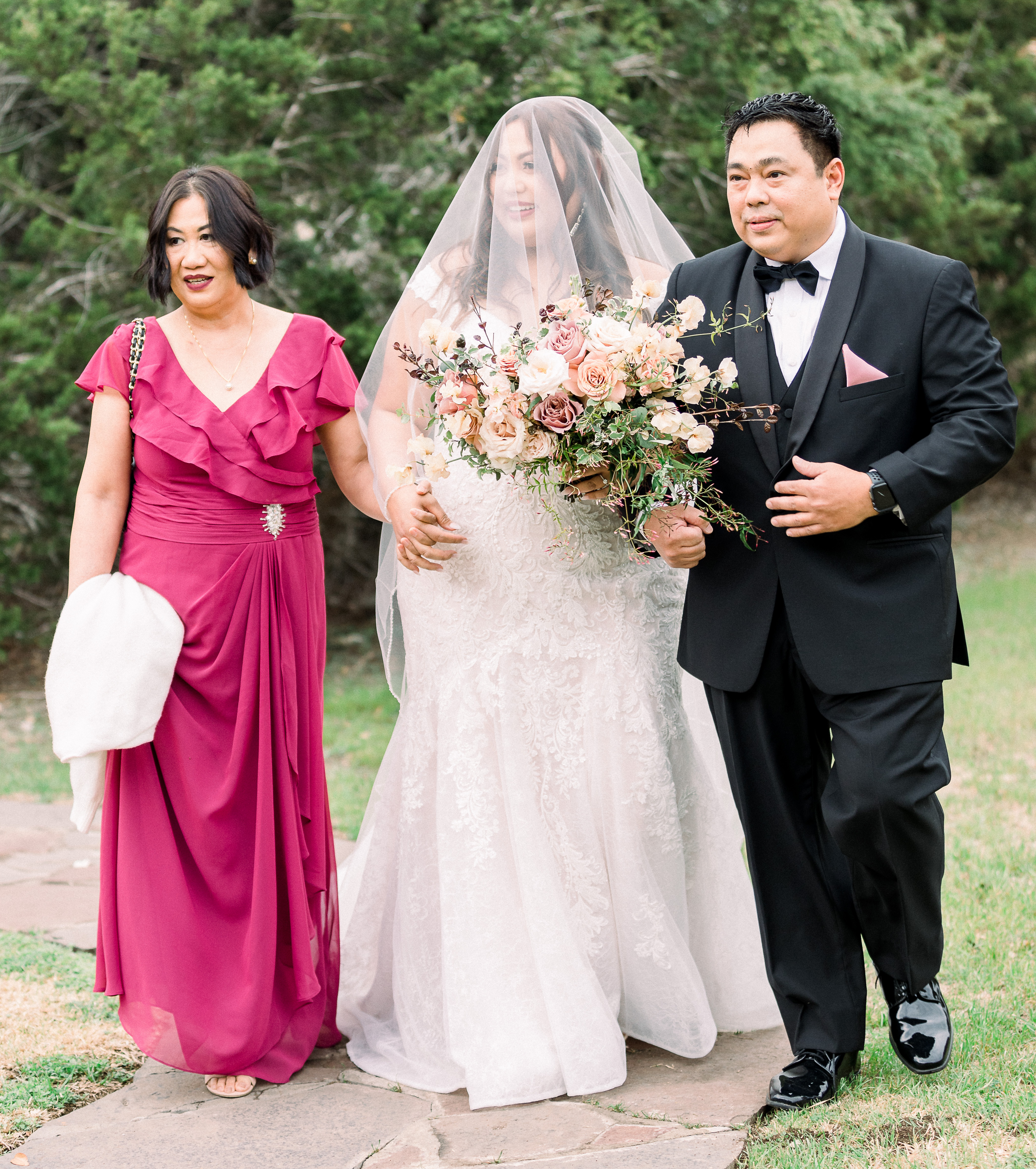 Bride walking in between her mother and father at her outdoor wedding ceremony in the Texas hill country. 