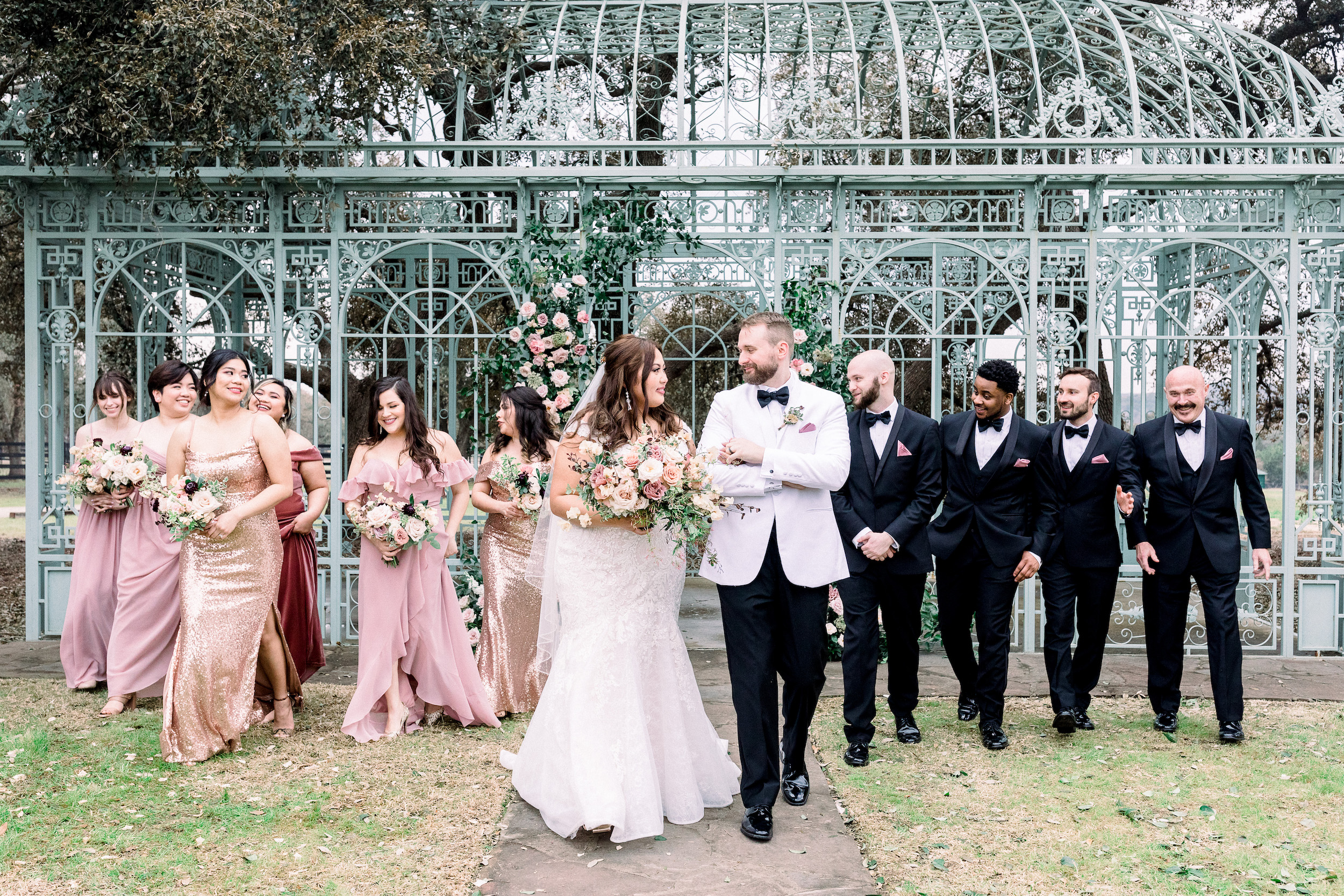 The bride and groom smile at each other while their wedding party is behind them.