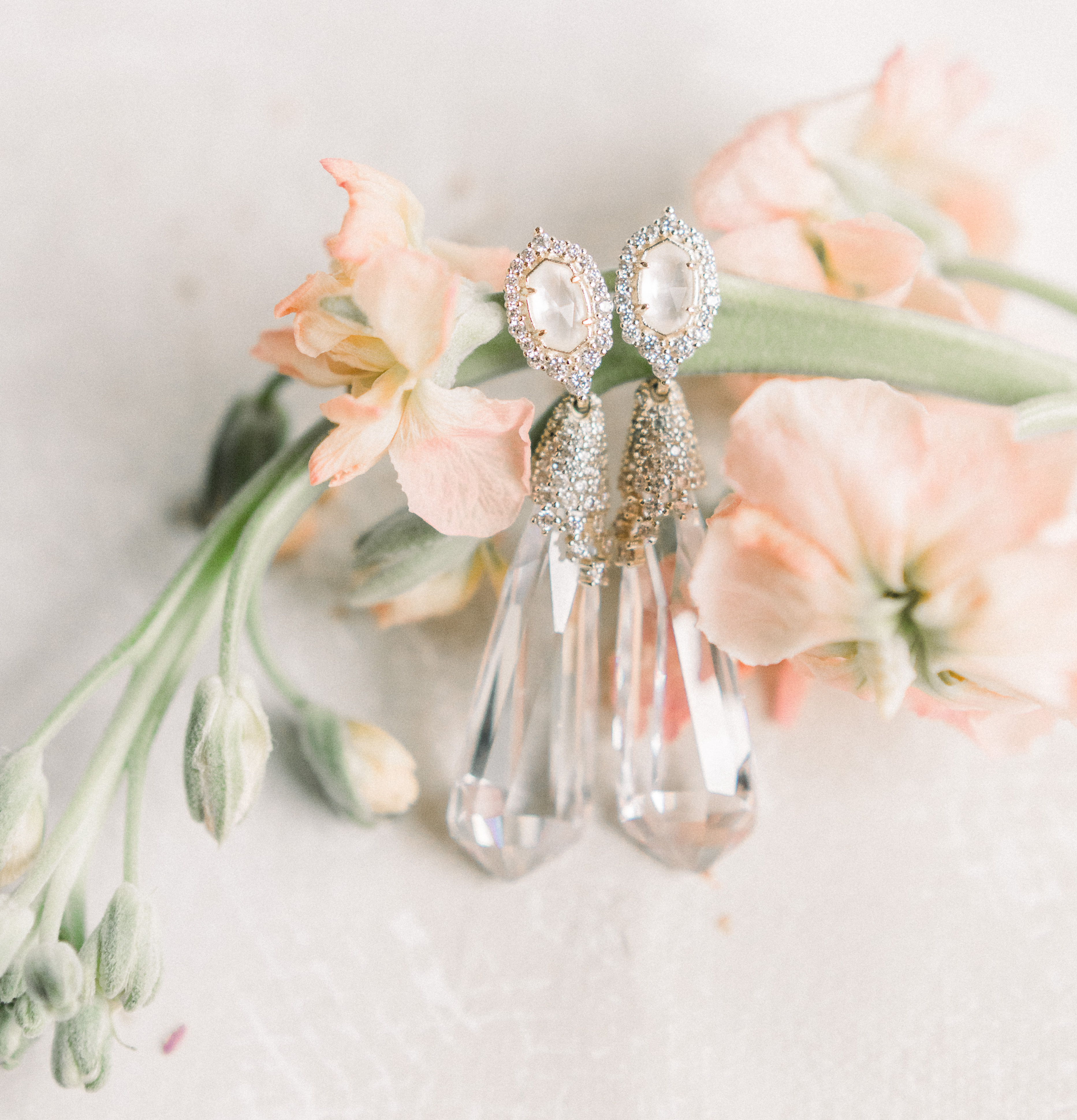 Teardrop earrings placed on a fresh floral stem atop a white surface at a sentimental wedding in the Texas hill country photographed by Anna Kay Photography.