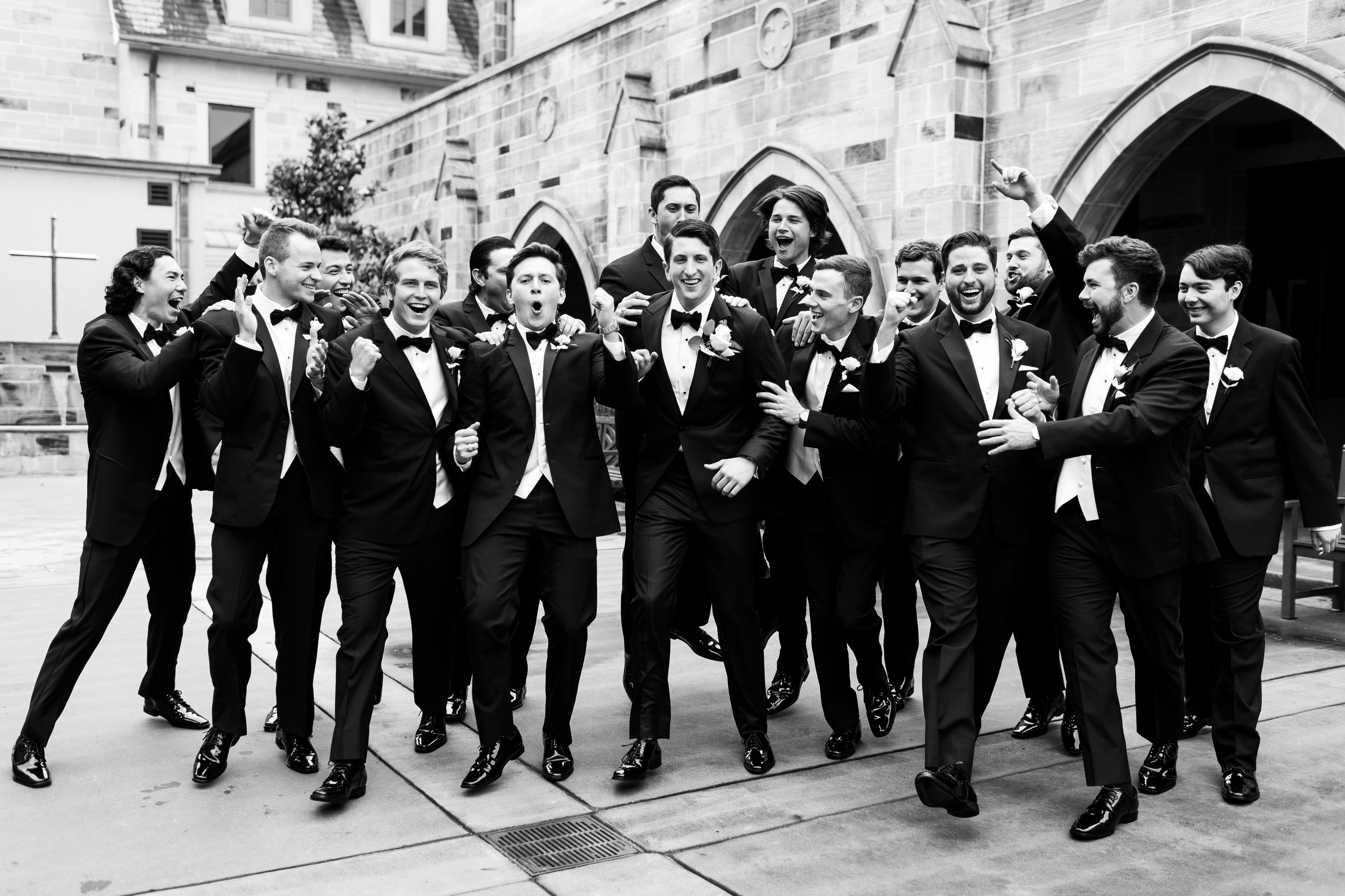 The groom and his groomsmen are all cheering in front of the cathedral.