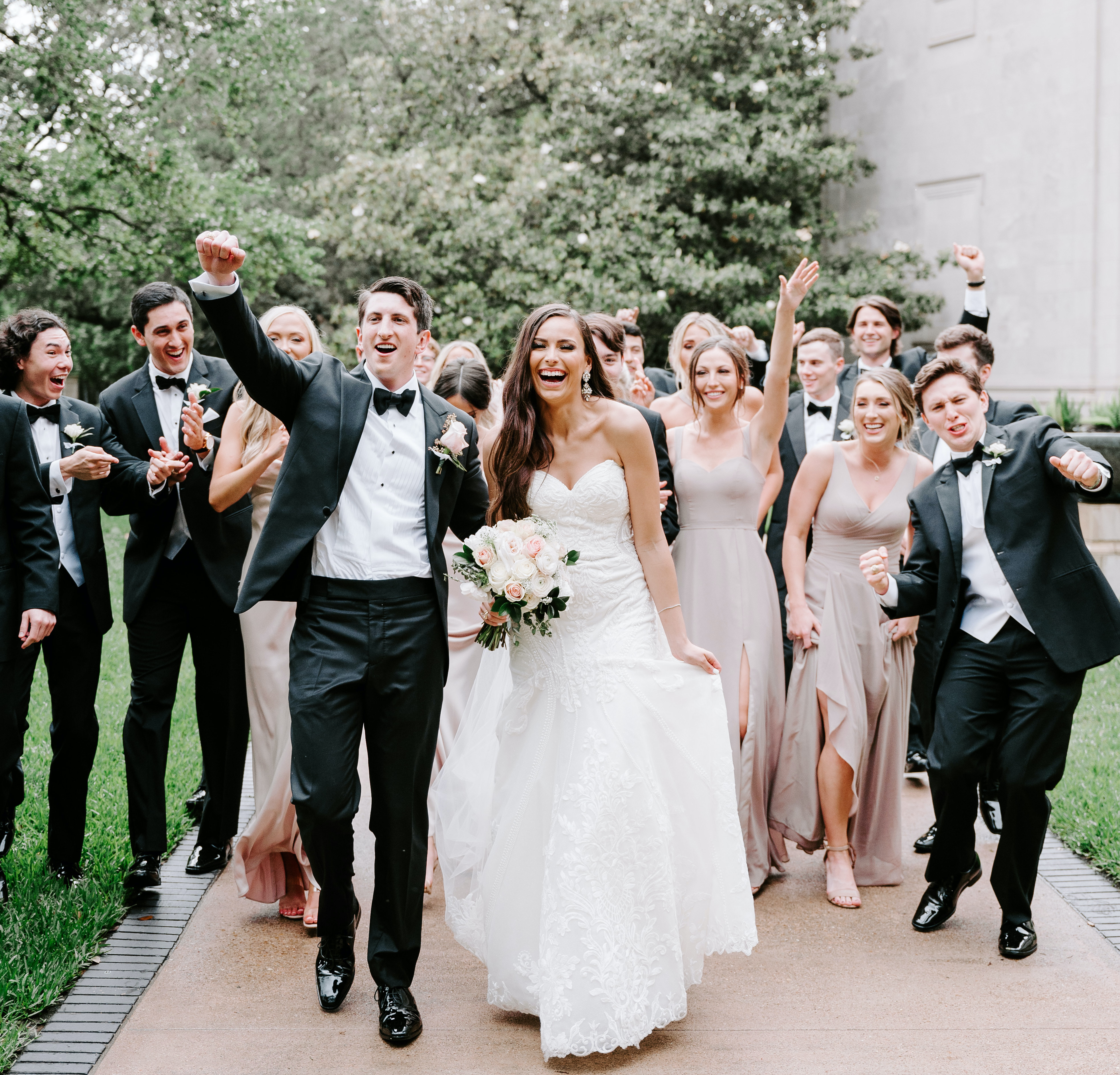 The bride and grom are cheering with their wedding party behind them.