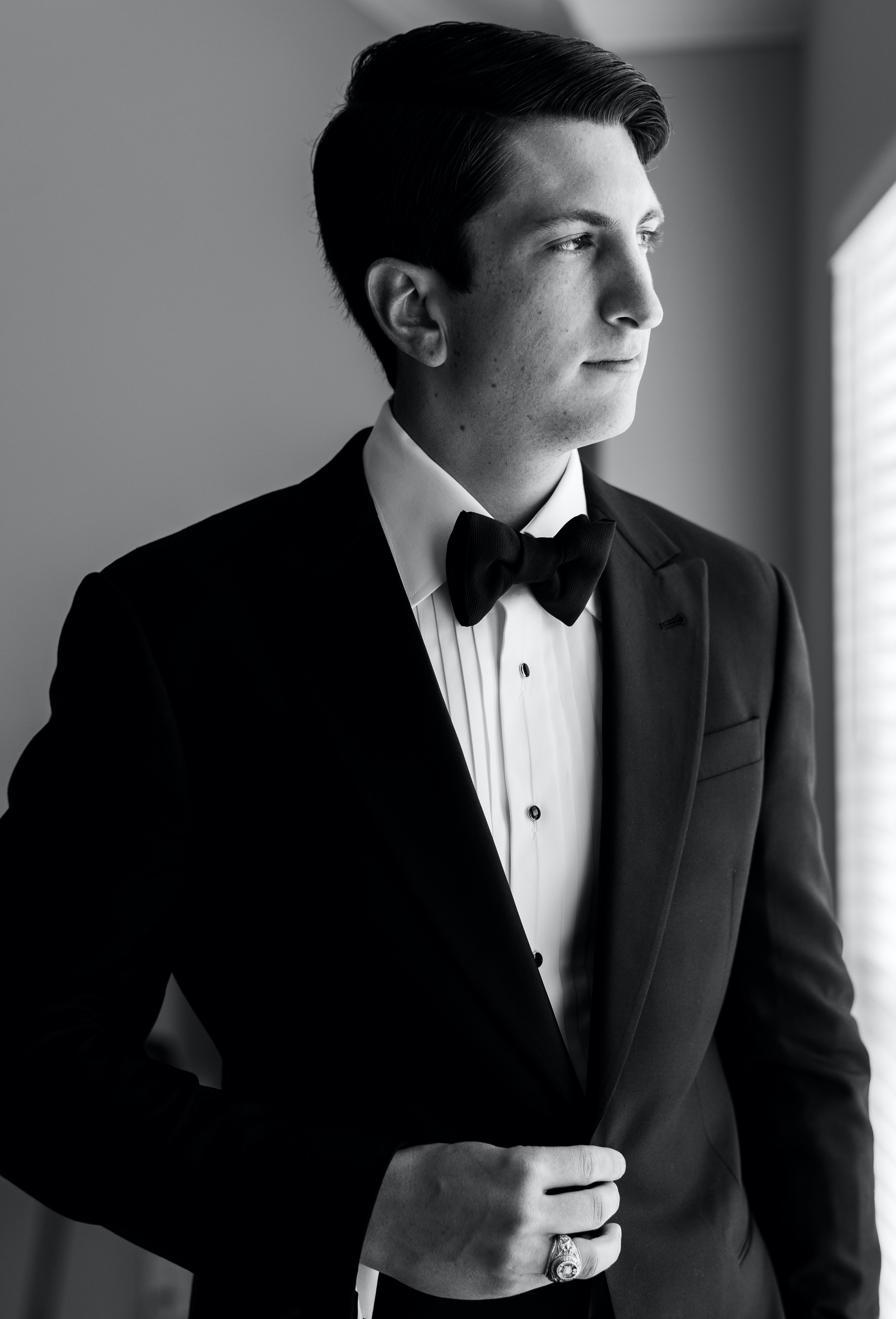 The groom looks out the window as he is getting ready for his elegant rainy wedding.