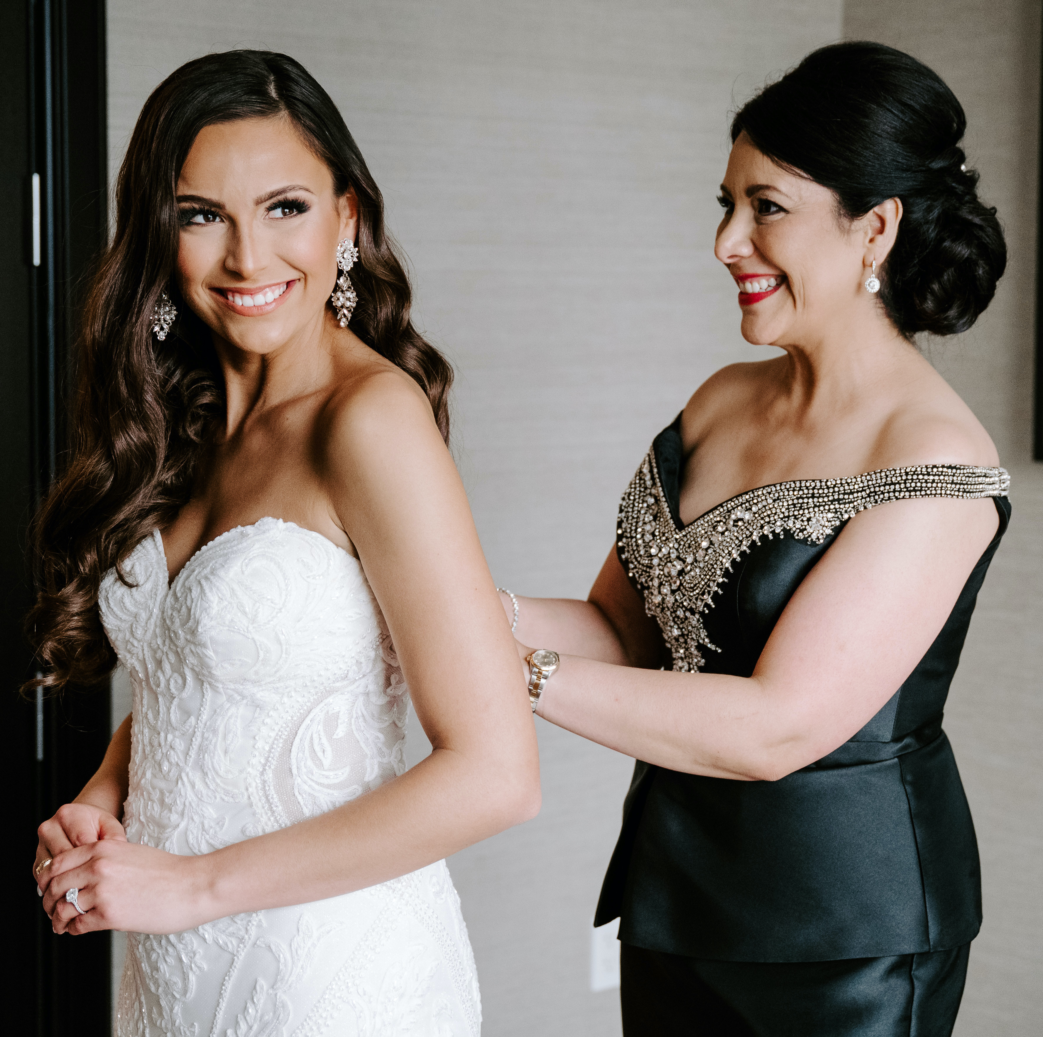 The bride's mom is helping her put on her wedding dress.