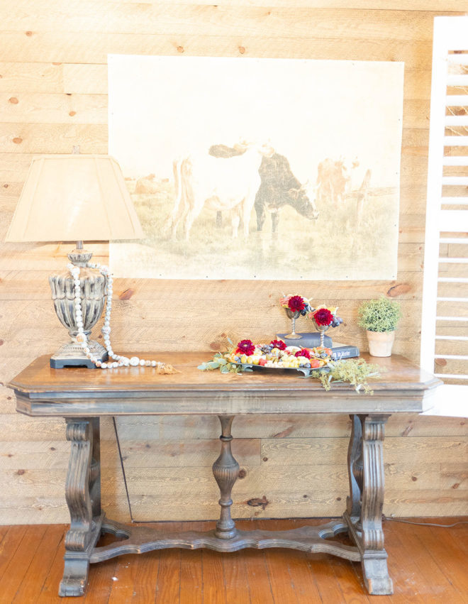 Wood table set with lamp, florals and metal tray with florals, nuts, cheese and grapes inside a guest suite at The Kendall. 