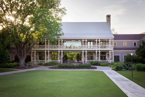 A front view of a hill coutry wedding venue with a big lawn and trees surrounding it.