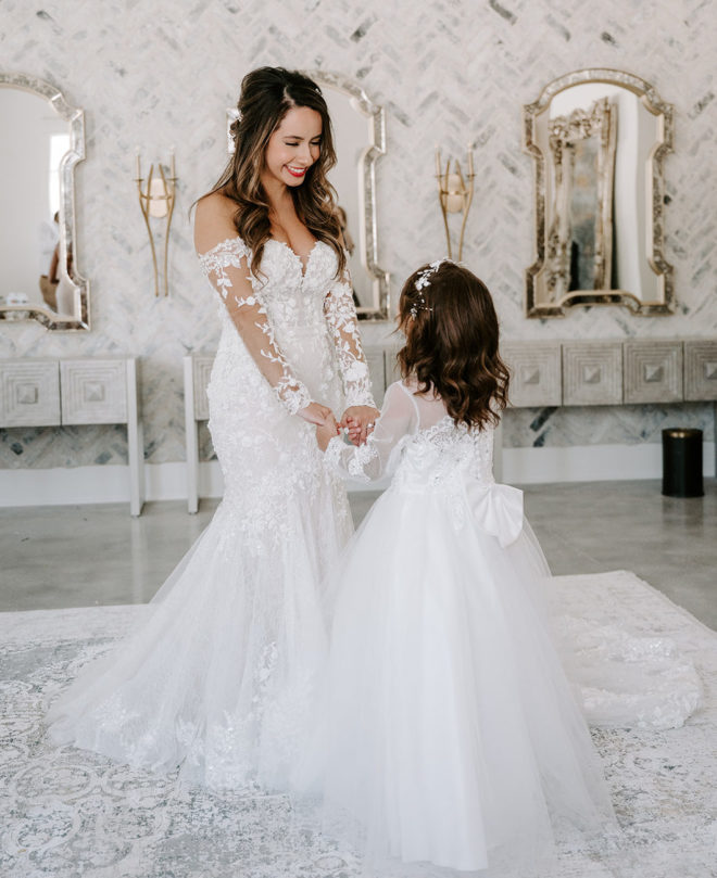 The bride holds the flower girl's hands and smiles down at her in the bridal suite at The Peach Orchard